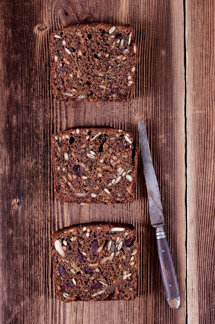 Drei Scheiben Bananenbrot mit Sonnenblumenkernen, Kürbiskernen, Cranberries, Apfelrübenkraut und Walnussmehl