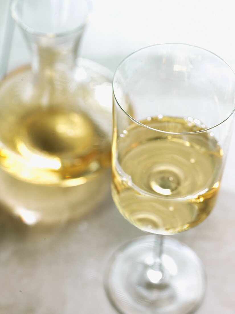 A glass of white wine with a wine caraffe