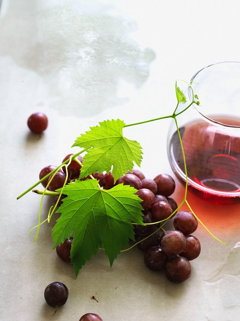 Rote Trauben mit Weinblättern und Glas Rotwein