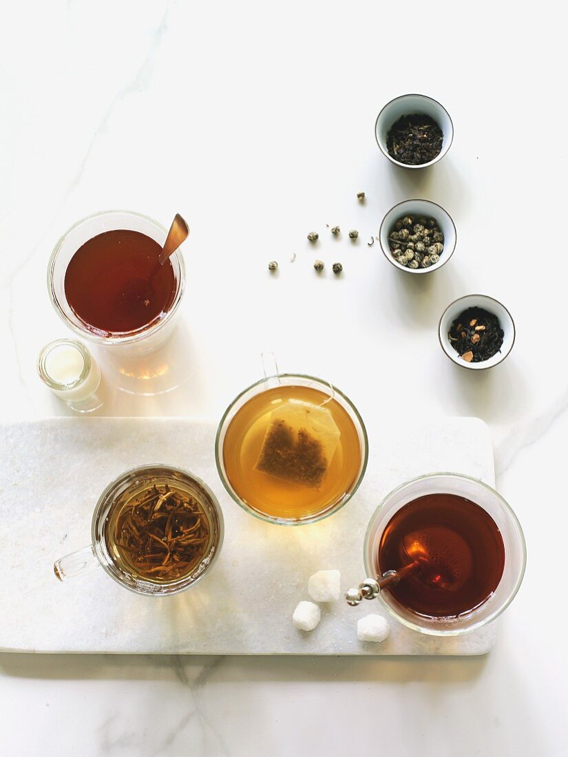 Assortment of teas in clear cups on white with tea leaves