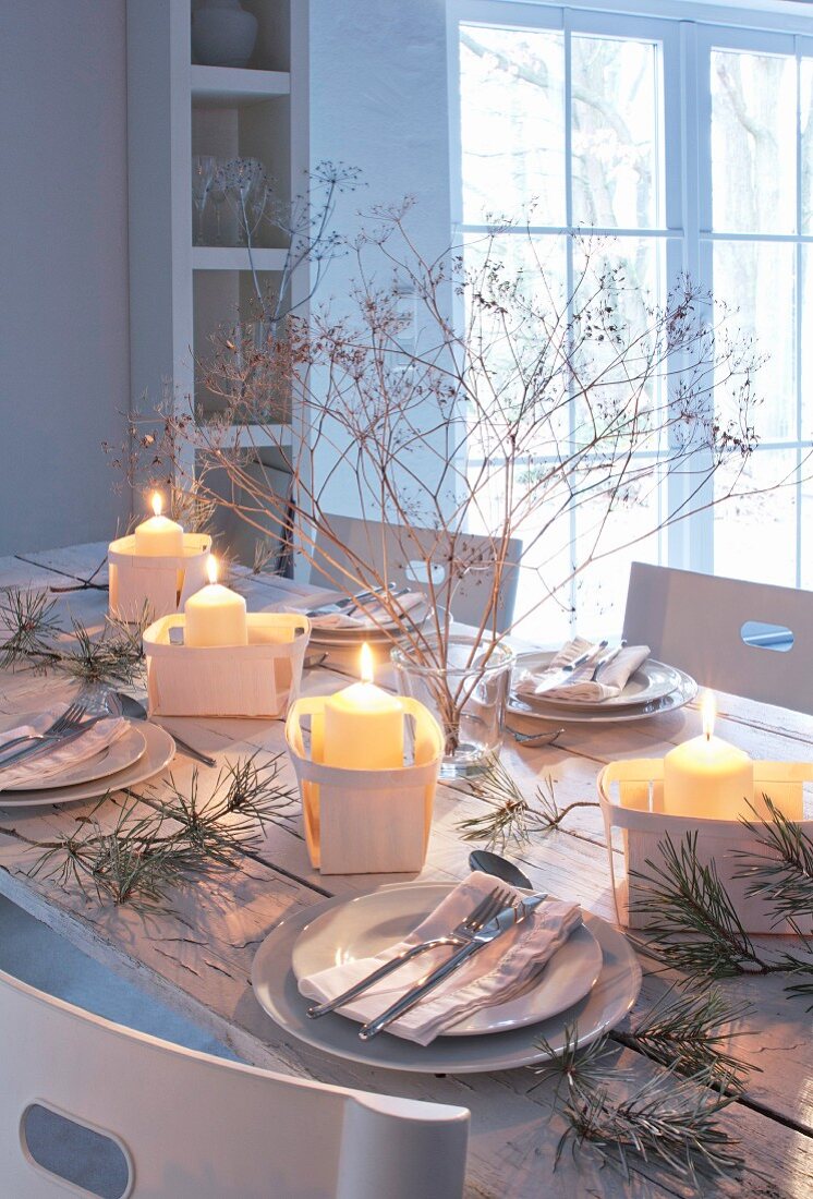 Wintry, romantic dinner table decorated with lit candles in chip wood baskets