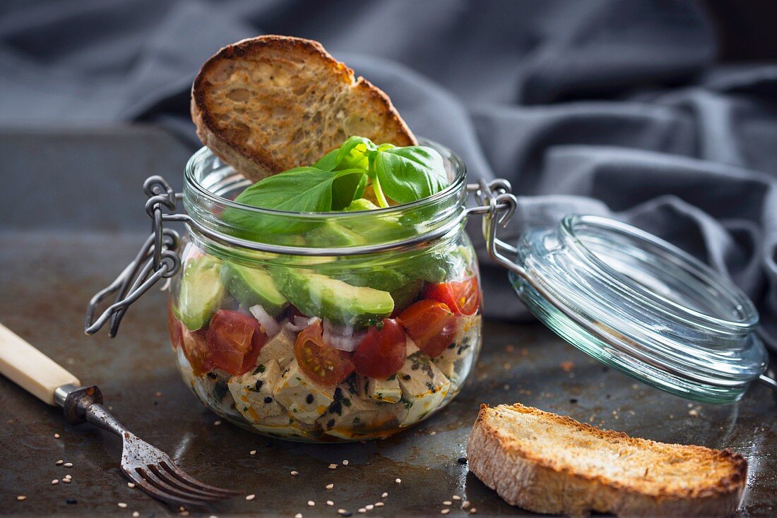 Marinated tofu with sesame seeds, tomatoes, shallots, avocado and toast in a glass jar