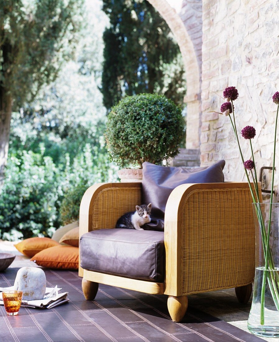 Elegant wicker armchair with leather seat cushion next to glass vase and brick wall