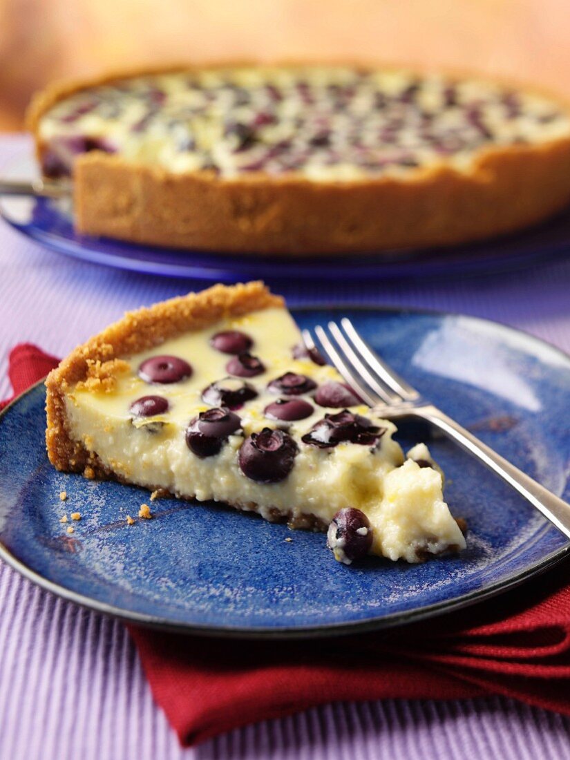 A slice of blueberry lemon pie on a plate with a whole pie in the background