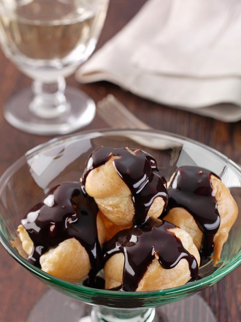 A dish of profiteroles with rich dark chocolate sauce editorial food