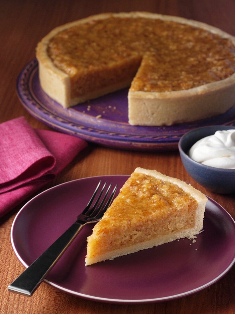 A slice of treacle tart on a plate with the whole tart behind