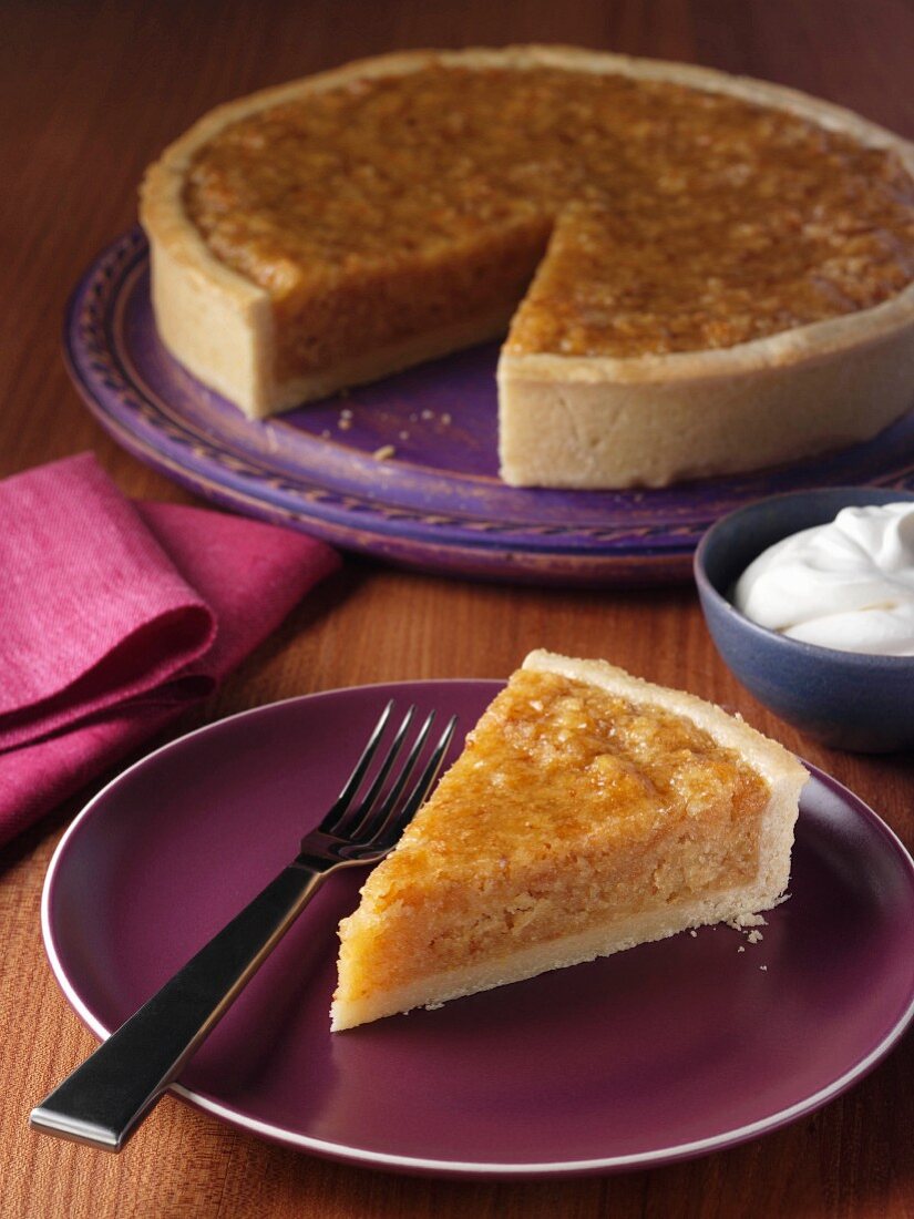 Ein Stück Treacle Tart (Siruptorte, England) auf Teller, ganze Torte im Hintergrund