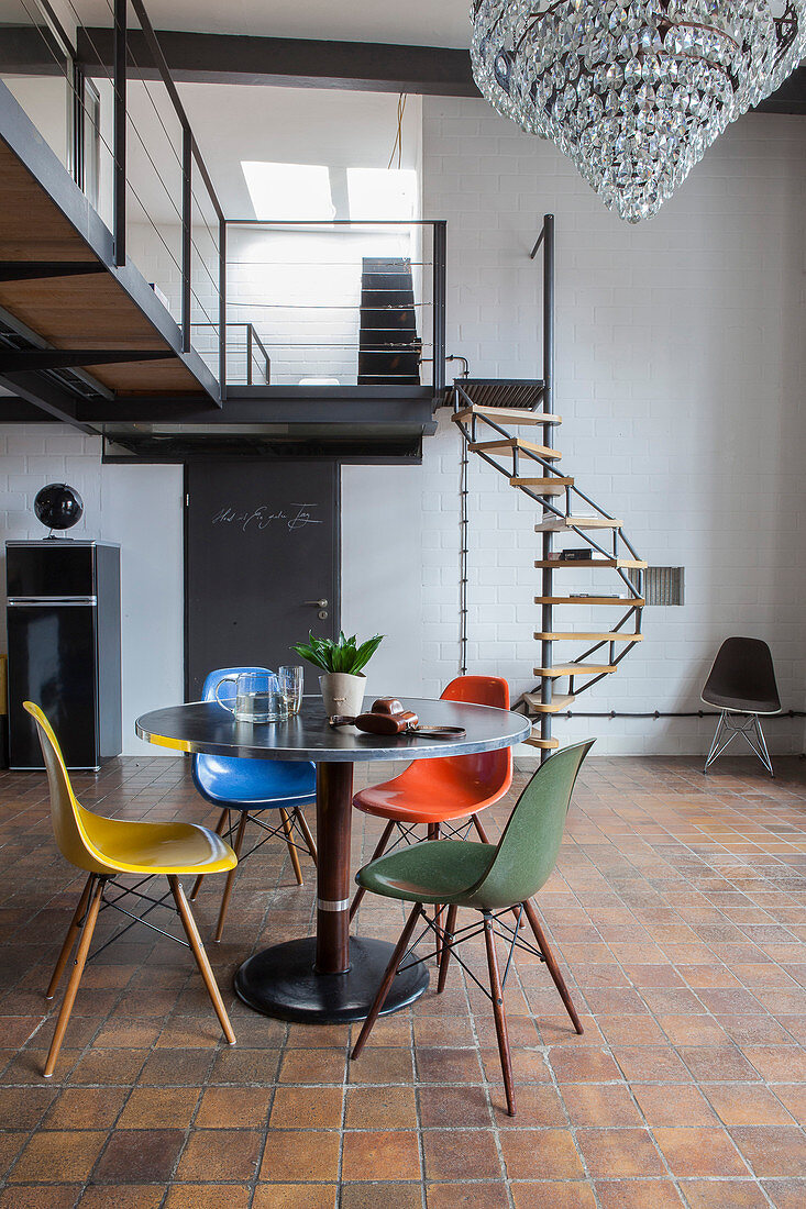 Round dining table and colourful designer chairs in industrial loft apartment