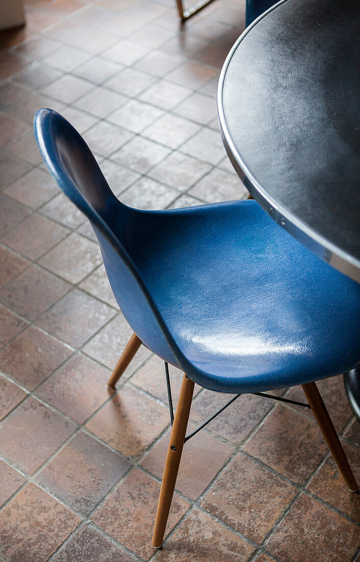 Blauer Designerstuhl vor rundem Tisch auf braunem Fliesenboden