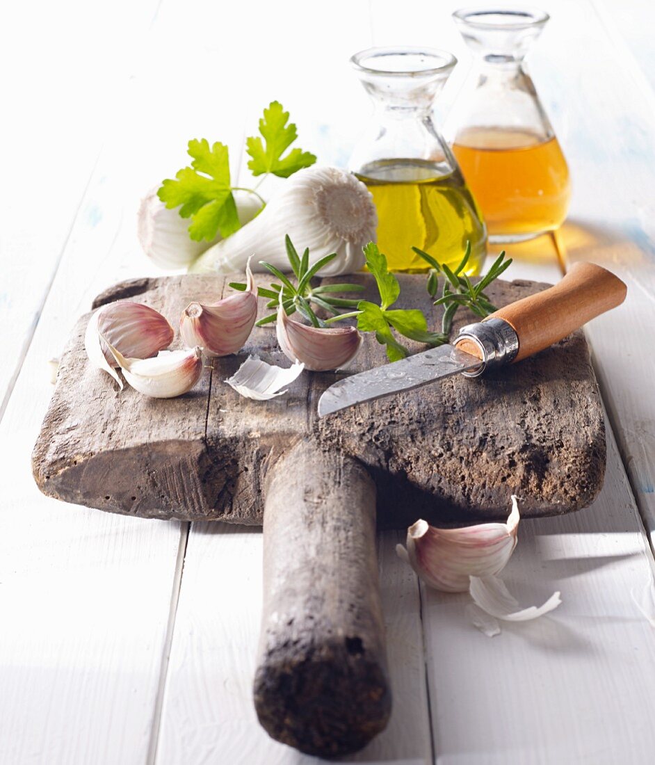 Cloves of garlic with oil, vinegar and a knife on an old wooden board