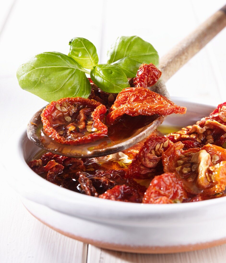 Dried tomatoes in olive oil with basil on a wooden spoon and in a bowl