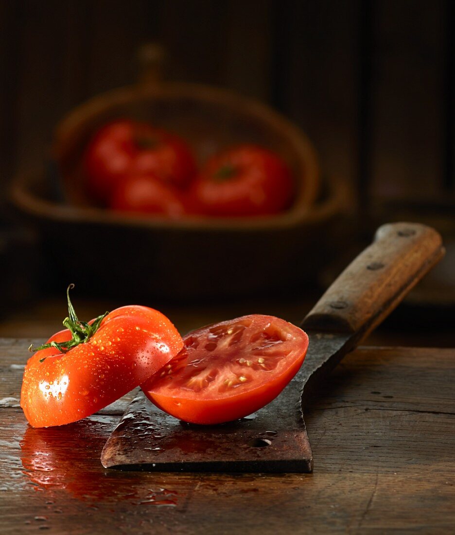 A halved tomato with water droplets on an old butchers knife