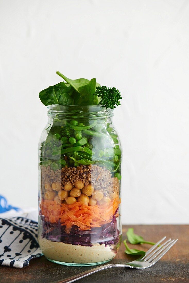 A quinoa salad with houmous and vegetables in a glass jar
