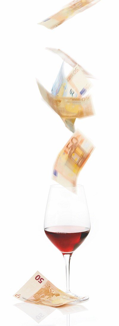 Banknotes falling into a glass of red wine to symbolise expensive wine prices