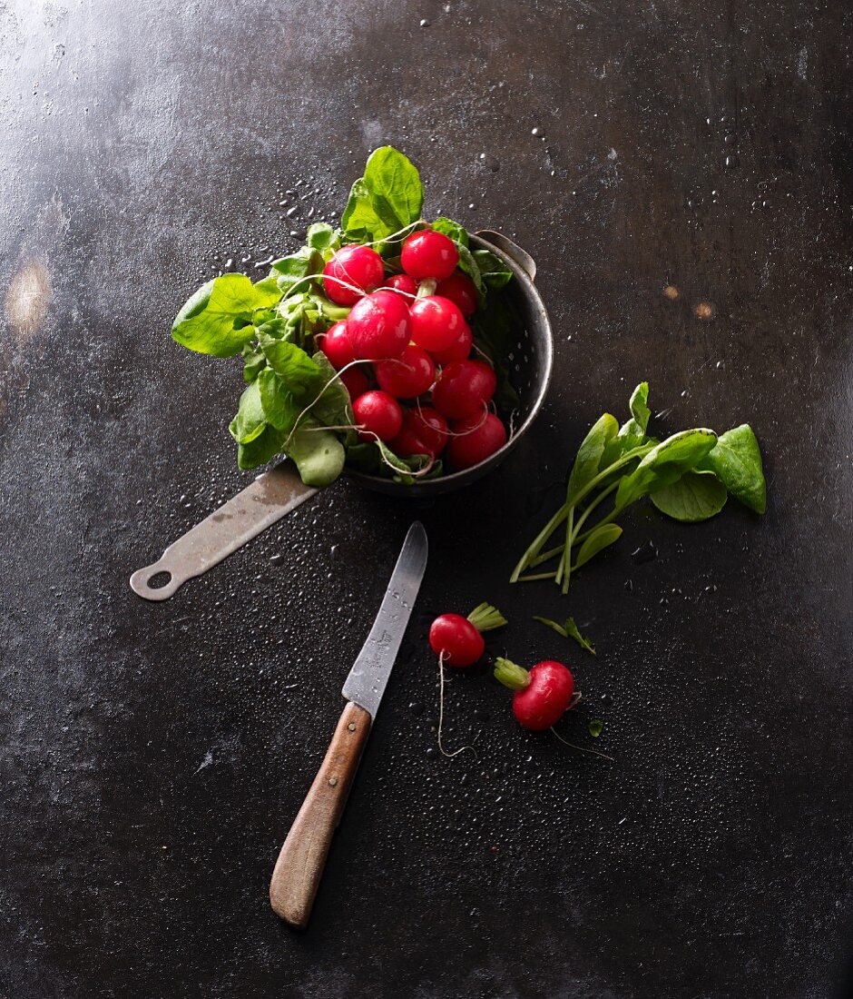 A colander with washed radishes and a knife on a black baking tray