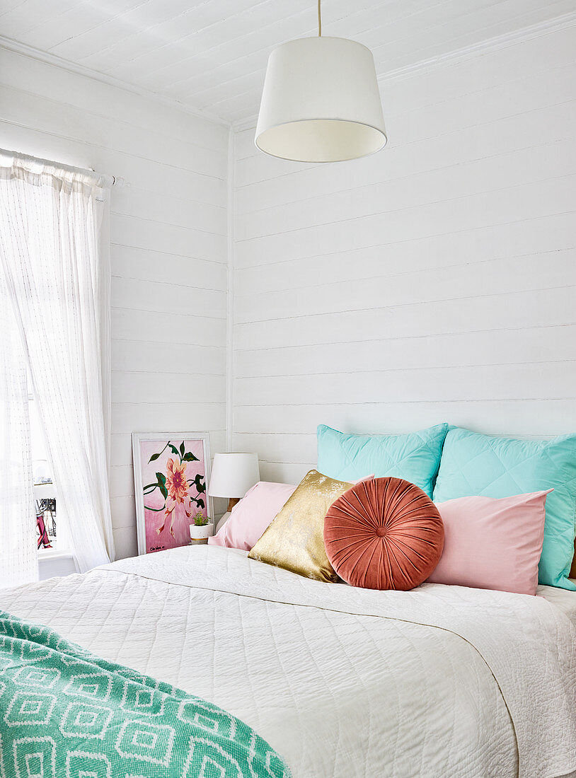 Colourful cushions on bed in bedroom with board wall