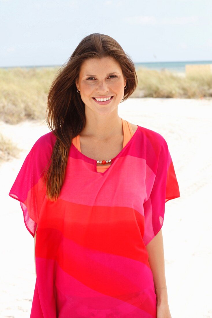 A brunette woman wearing a pink tunic on the beach