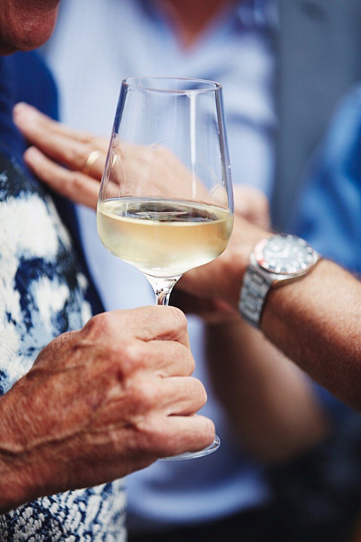 A hand holding a glass of white wine at Feinkost Urbanek on the Naschmarkt market in Vienna, Austria