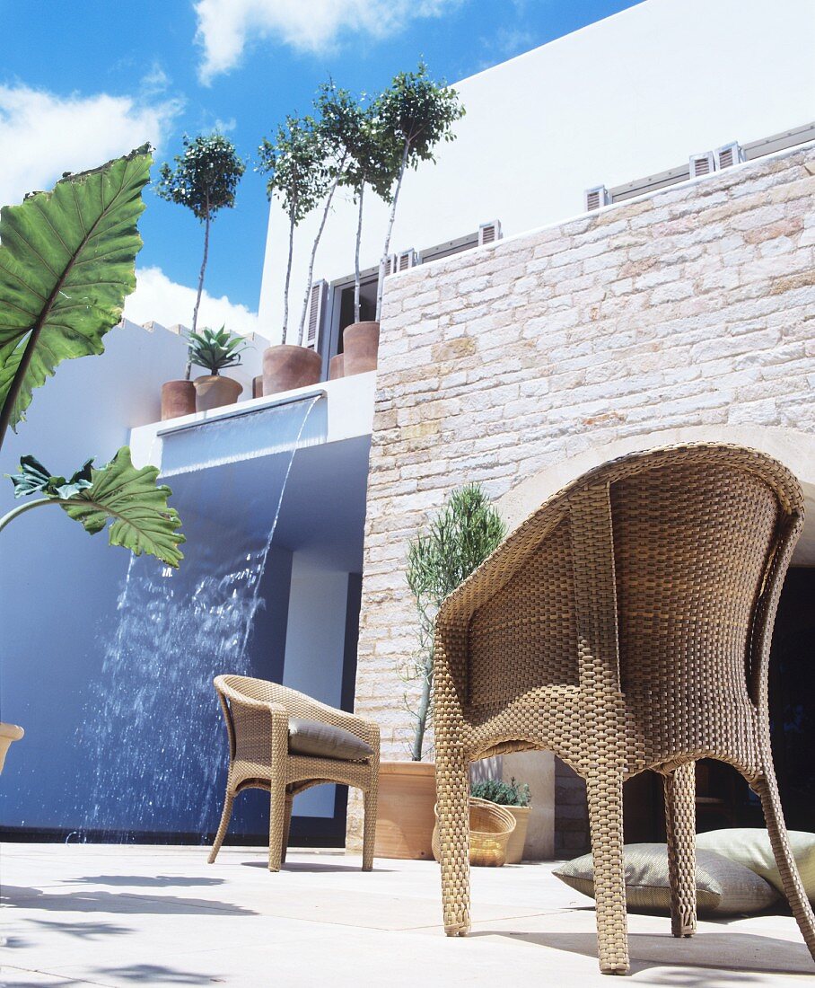 Wicker chair outside modern house with stone wall and waterfall