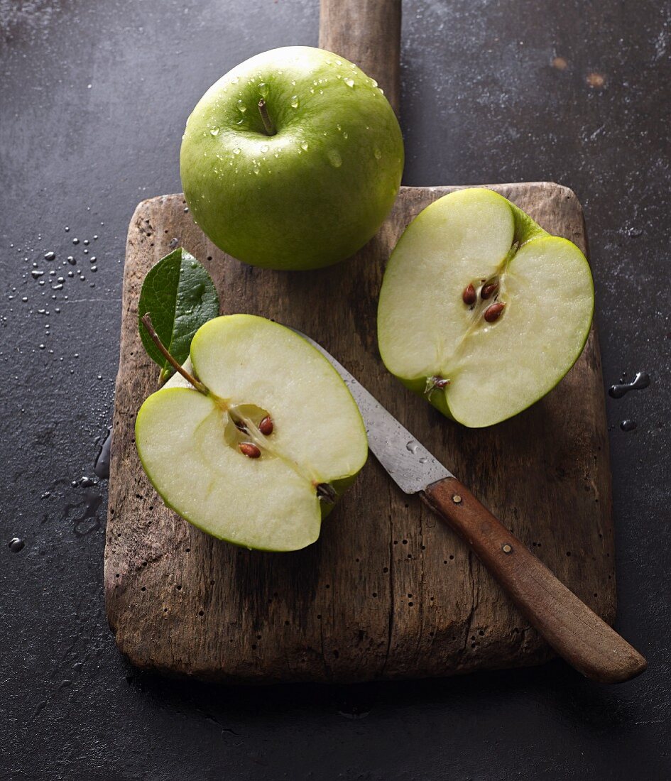 Granny Smith apples, whole and halved, on an old wooden board with a knife