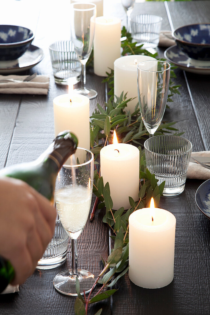 Hand pouring Champagne into glass on festively set table