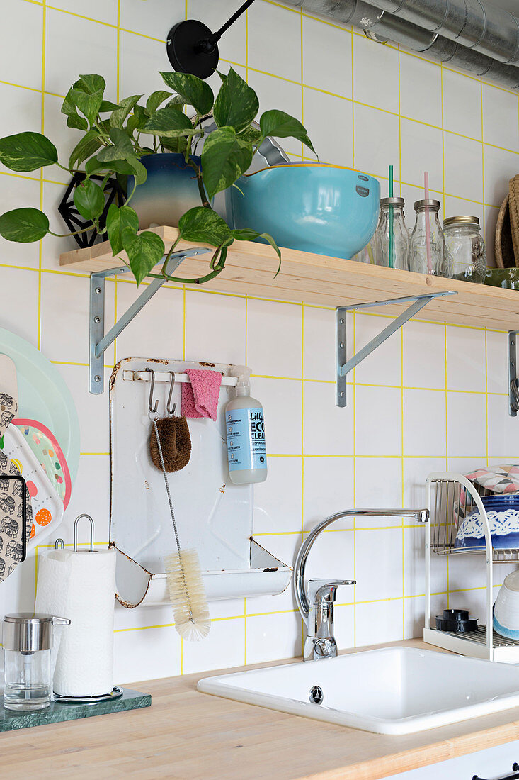 Bracket shelf on tiled wall with yellow grouting above sink