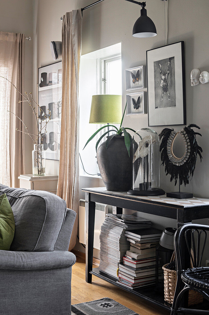 Books, urn, animal skull and mirror on console table and grey sofa in foreground in living room