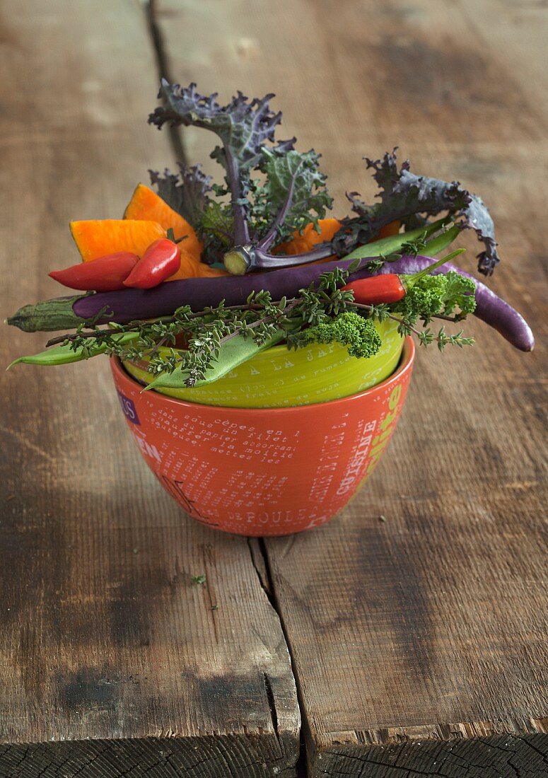 A vegetable bowl containing kale, chillis, pumpkin and long, thin aubergines