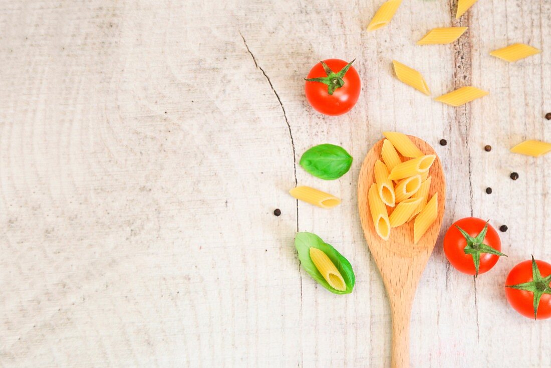 Penne pasta on a wooden spoon with fresh basil and tomatoes