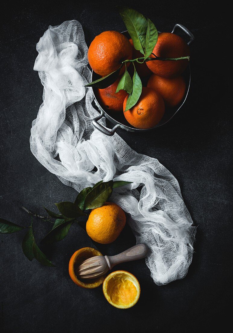 Orangen mit Blättern in Schüssel, weisses Tuch und Zitruspresse