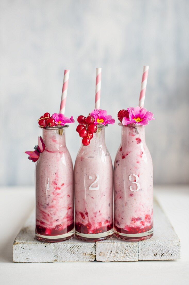 Beerenjoghurt in kleinen Flaschen, garniert mit Johannisbeeren und Blüten