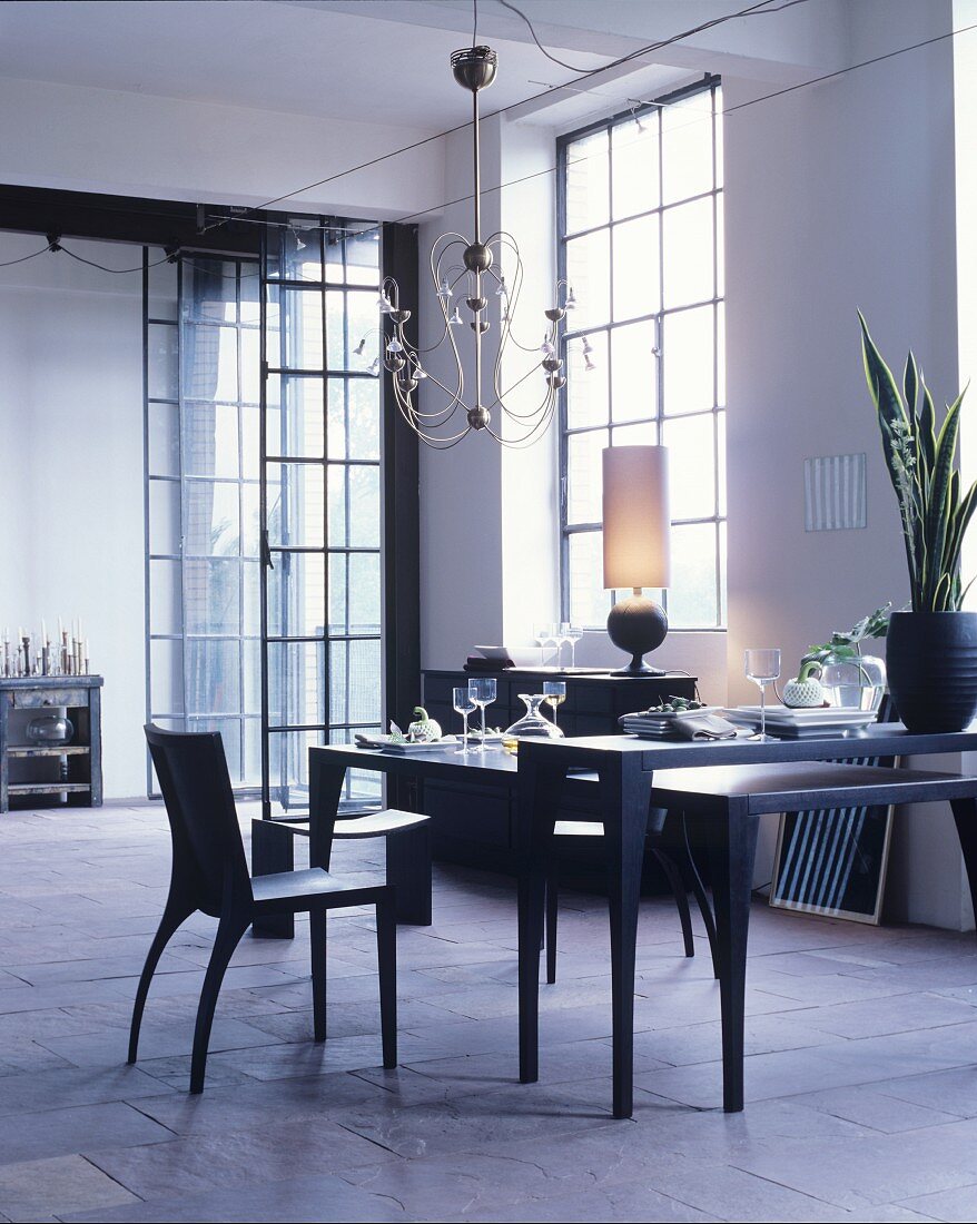 Black dining table in loft apartment with industrial windows and stone floor