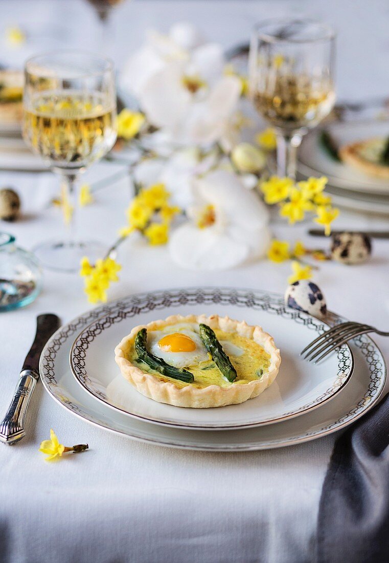 Asparagus quiche with fried quail egg on a dining table set for Easter