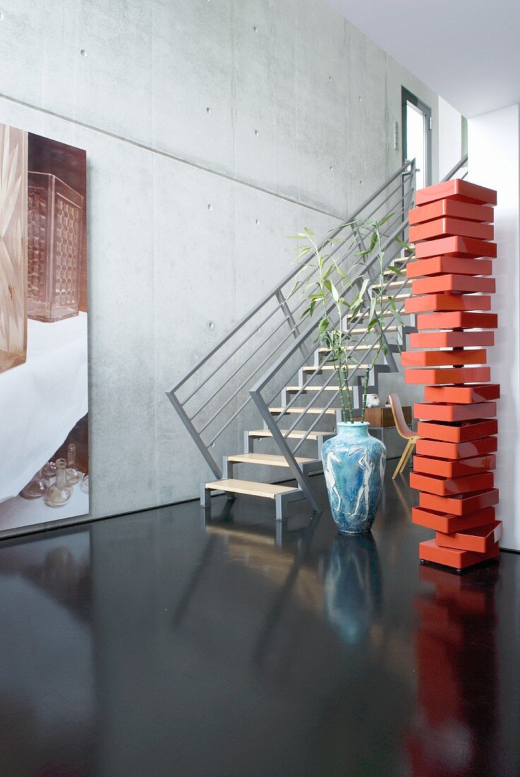 Rote Skulptur und schwebende Treppe auf schwarzem Boden