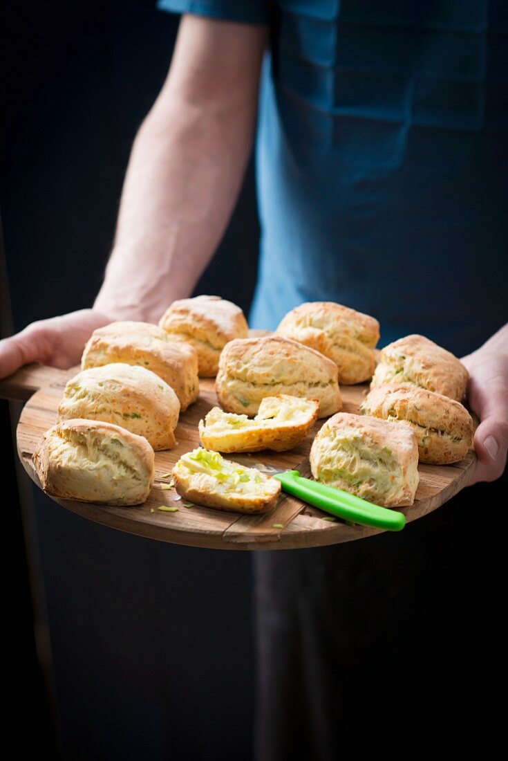 A person serving scones on a wooden plate
