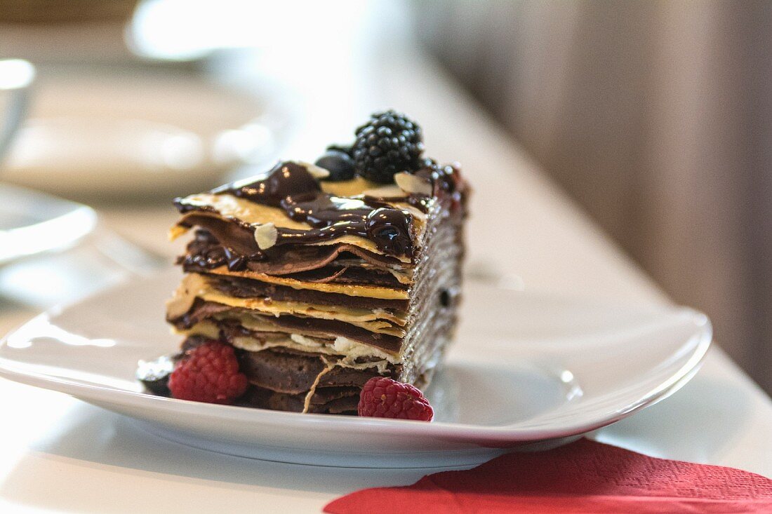 A slice of pancake cake with berries and chocolate sauce