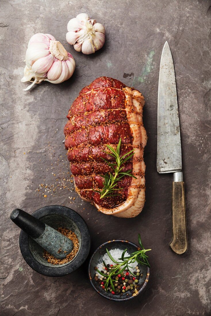 Raw roast beef Rump, seasonings and knife on dark stone slate background