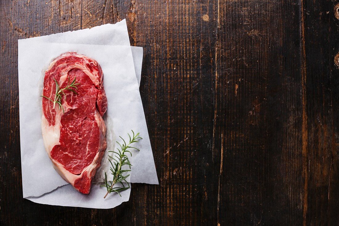 Raw fresh marbled meat Black Angus Steak and rosemary on dark wooden background
