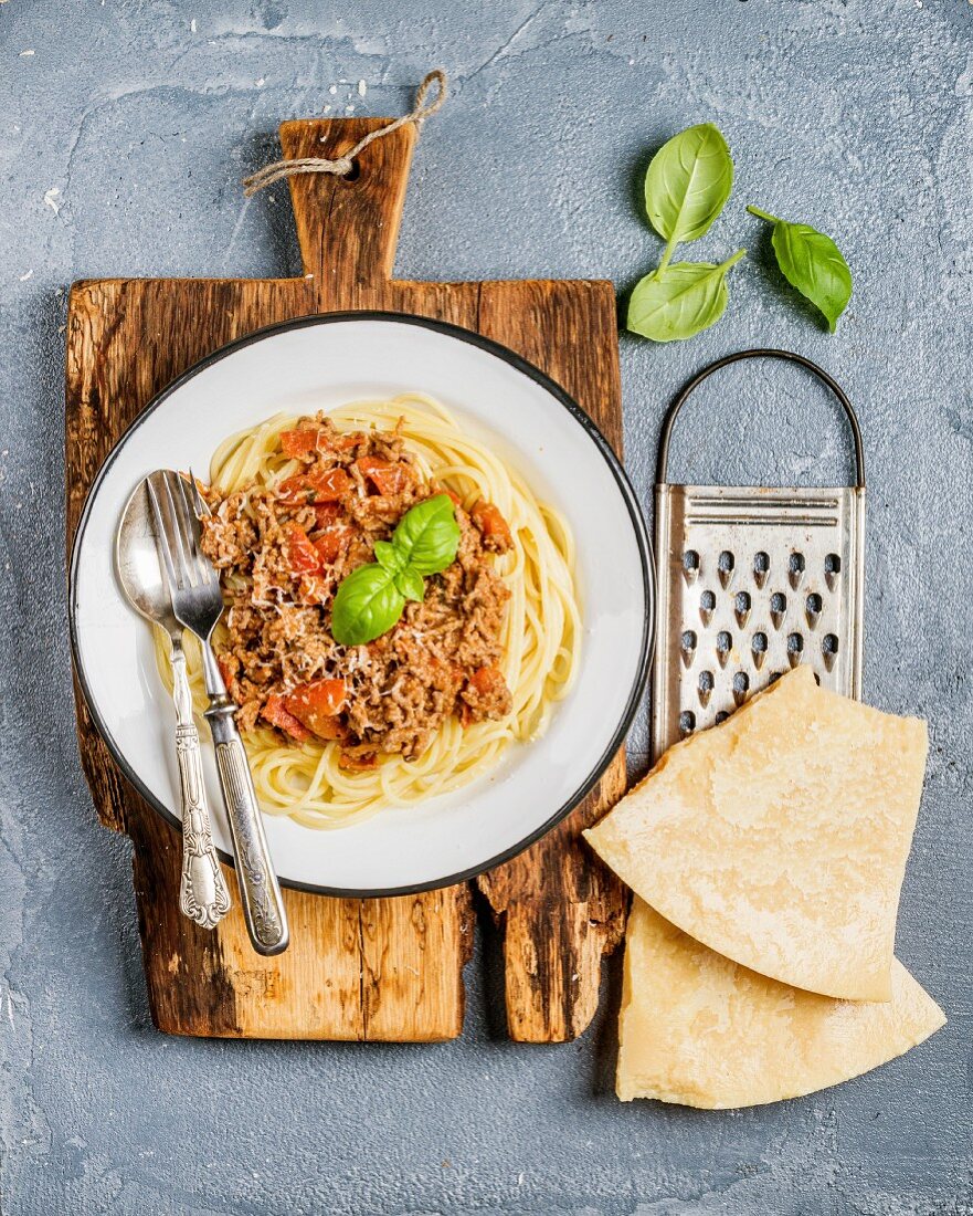 Spaghetti Bolognese auf Teller und rustikalem Holzbrett, daneben Parmesan und Reibe