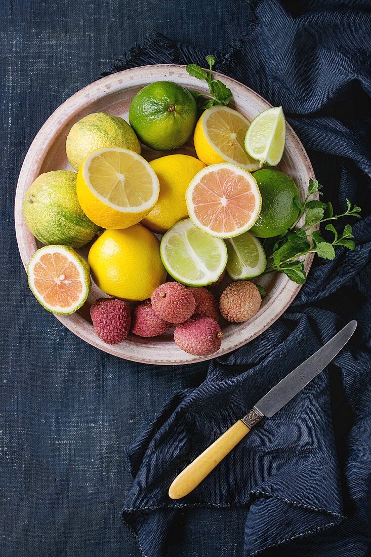 Variety of whole and sliced citrus fruits pink tiger lemon, lemon, lime, mint and exotic lichee on ceramic plate