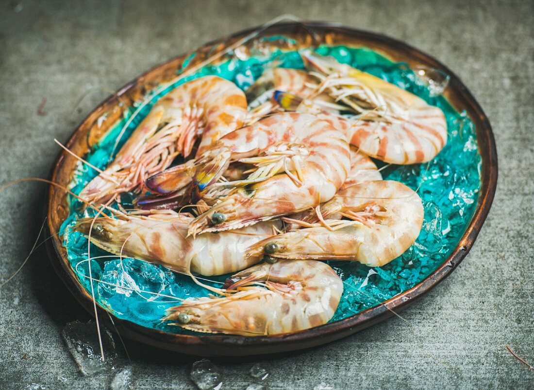 Raw uncooked tiger prawns on chipped ice in turquoise blue tray