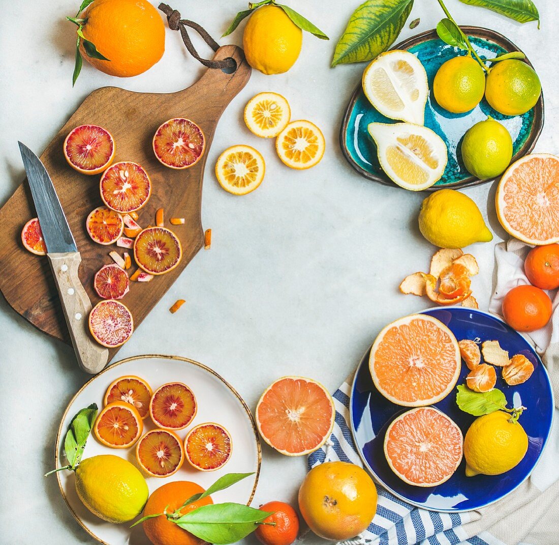 Natural fresh citrus fruits on wooden rustic board, colorful ceramic plates over grey marble table background