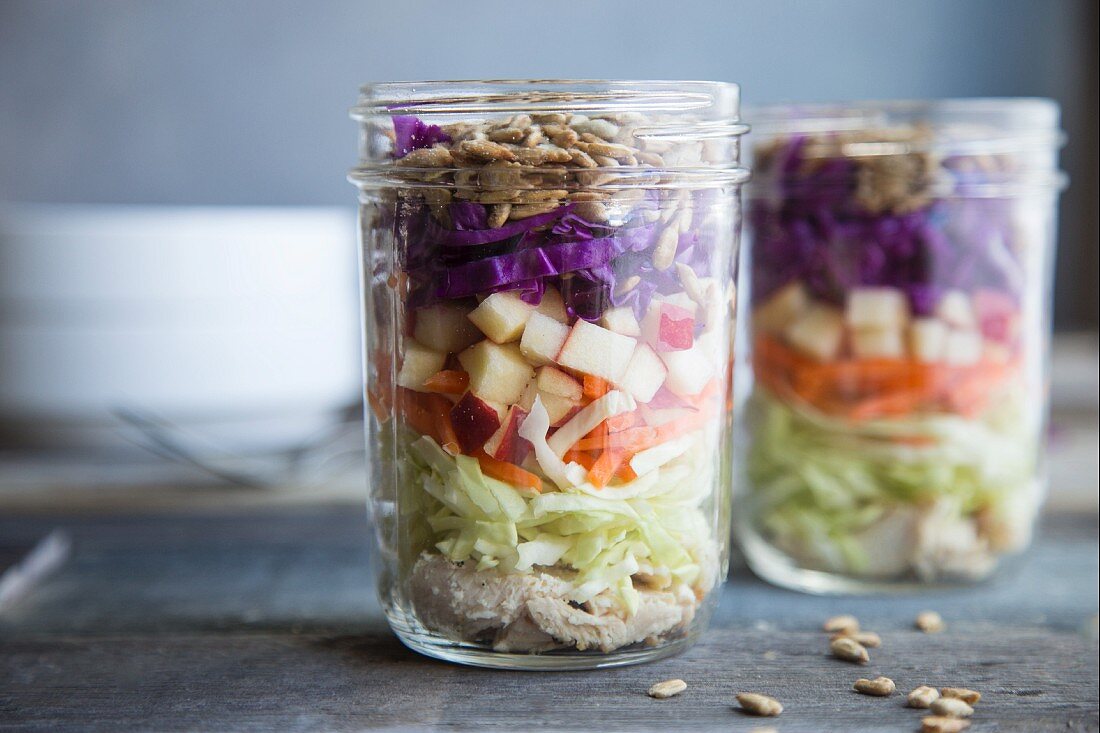 Layered salad with chicken, carrot, apple, red cabbage, kale and sunflower seeds in a glass jar