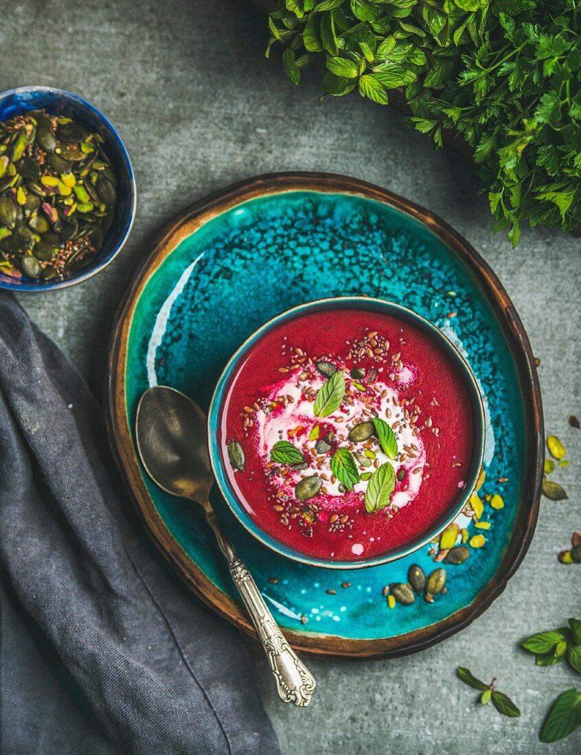 Spring detox beetroot soup with mint, chia, flax and pumpkin seeds on bright blue ceramic plate