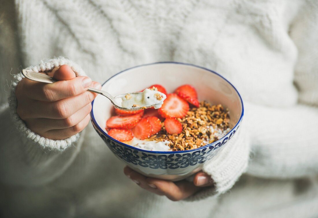 Healthy breakfast greek yogurt, granola and strawberry bowl in hands of woman