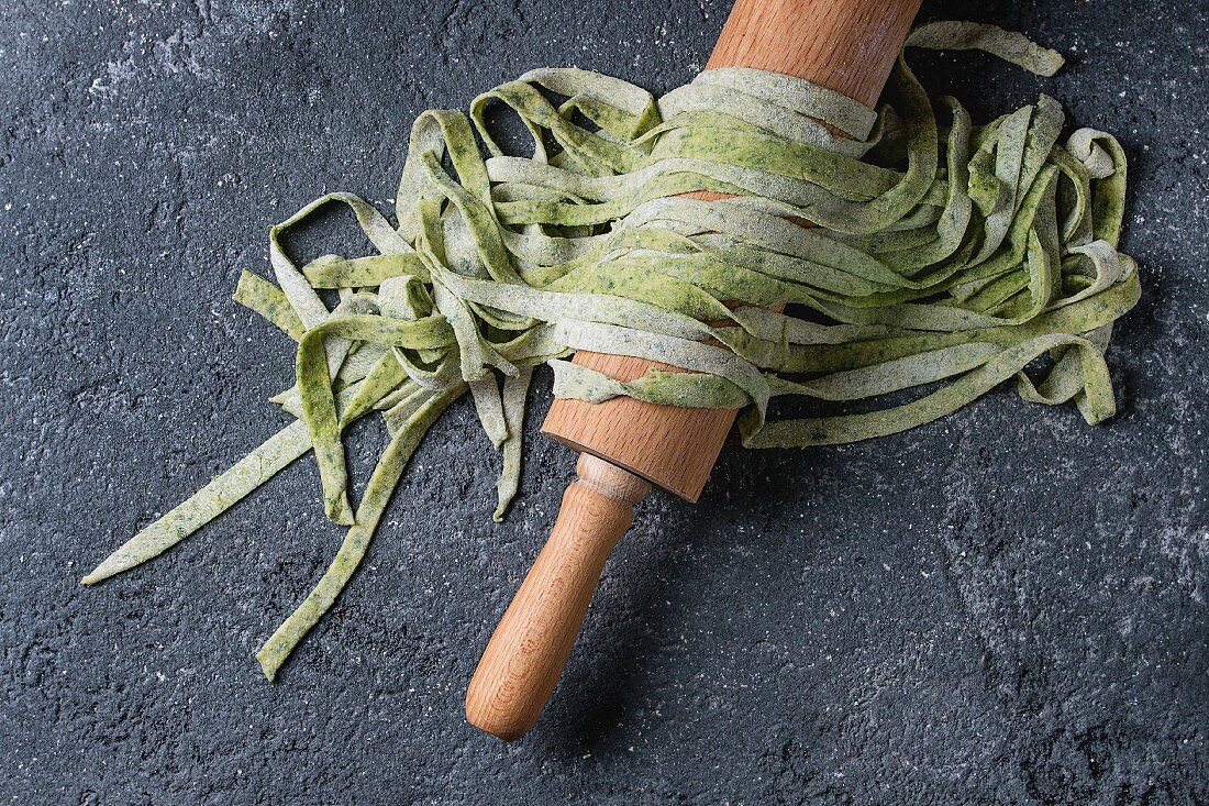 Fresh raw uncooked homemade green spinach pasta tagliatelle on wooden rolling pin