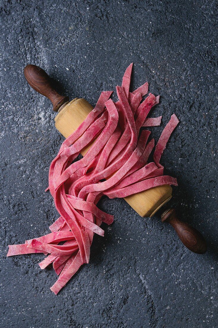 Fresh raw uncooked homemade pink beetroot pasta tagliatelle on wooden rolling pin