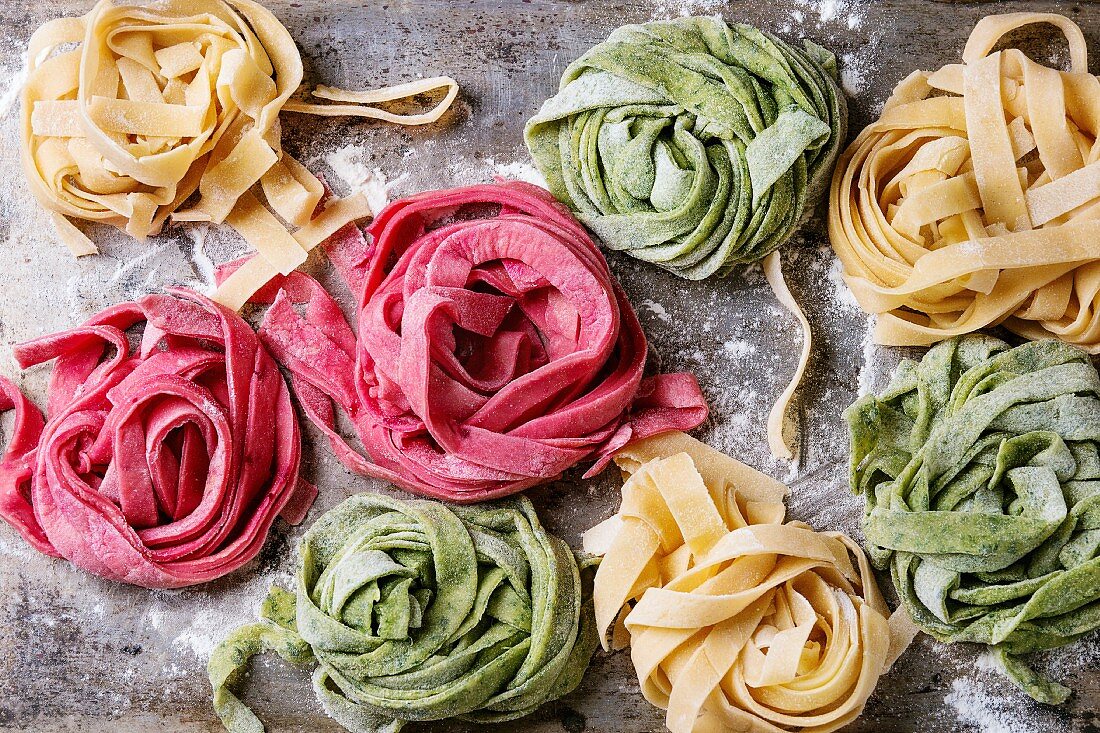 Variety of colored fresh raw uncooked homemade pasta tagliatelle green spinach, pink beetroot and yellow
