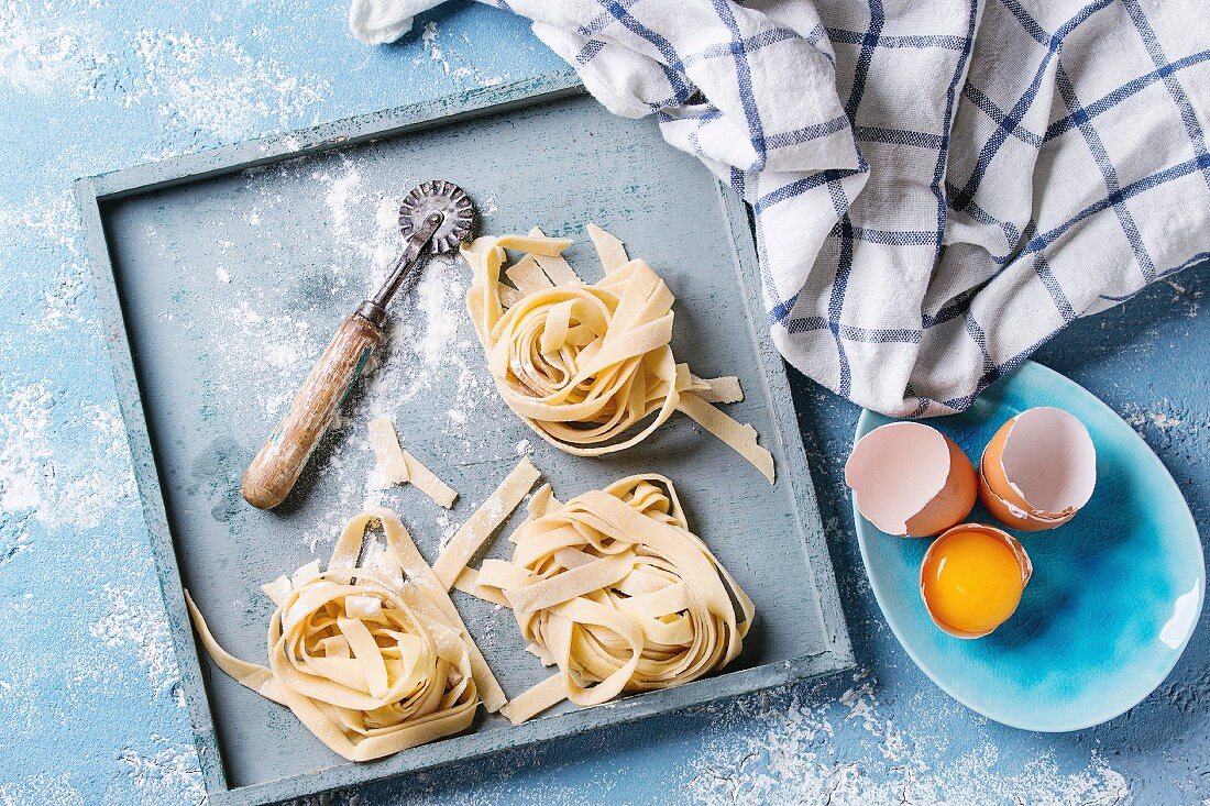 Fresh raw uncooked homemade twisted pasta tagliatelle with egg yolk and pasta cutter in wooden tray