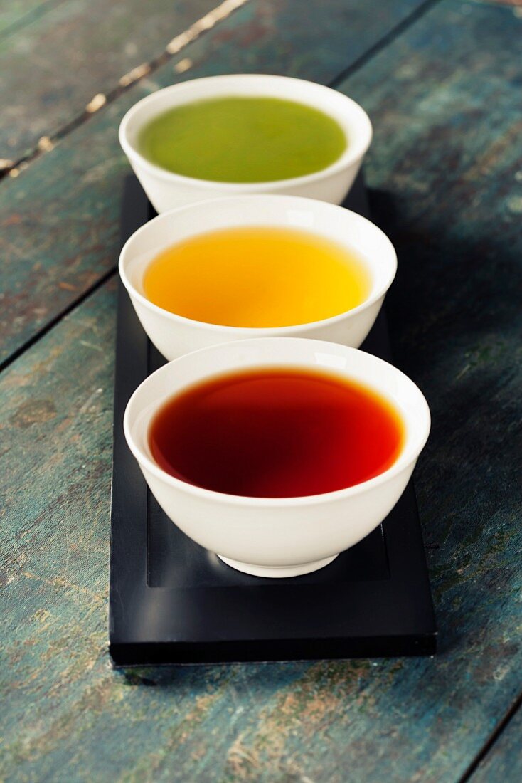 Tea concept. Different kinds of tea (black, green and matcha tea) in ceramic bowls on wooden background